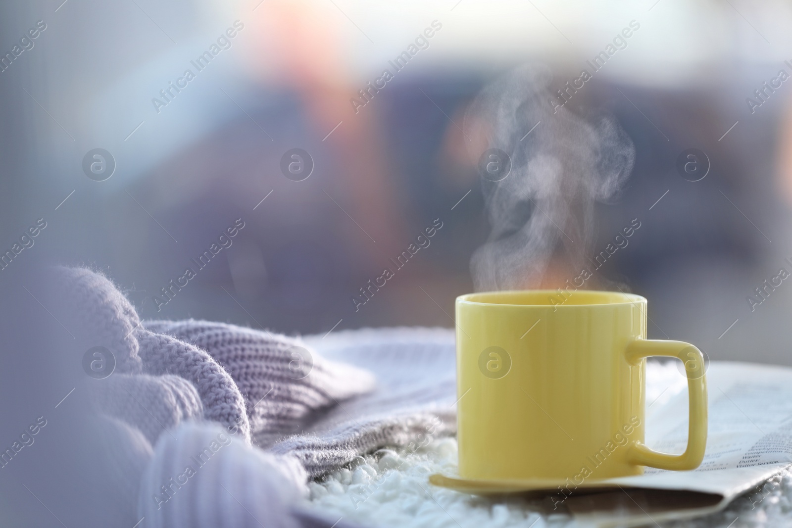 Photo of Cup of coffee, newspaper and knitted sweater near window in morning. Space for text