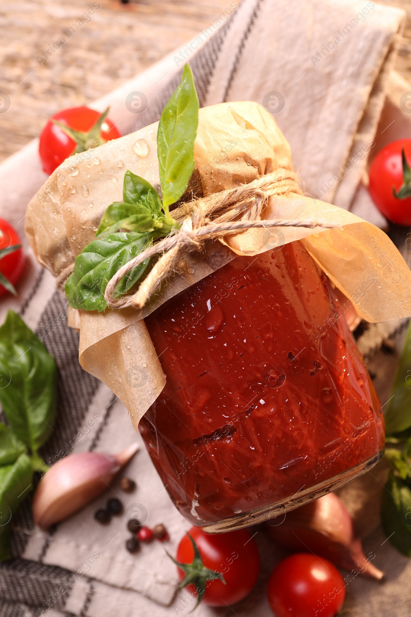 Photo of Jar of tasty tomato paste with water drops and ingredients on wooden table, flat lay