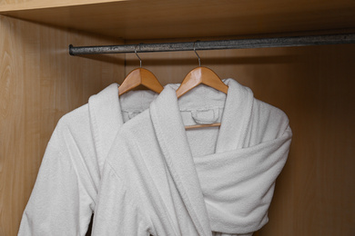 Photo of Fresh white bathrobes hanging in wooden closet