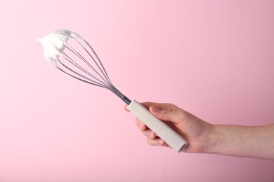 Photo of Woman holding whisk with whipped cream on pink background, closeup