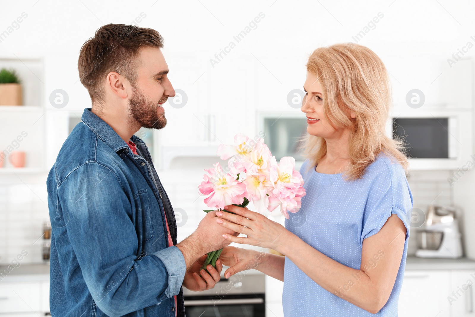 Photo of Young man congratulating his mature mom in kitchen. Happy Mother's Day