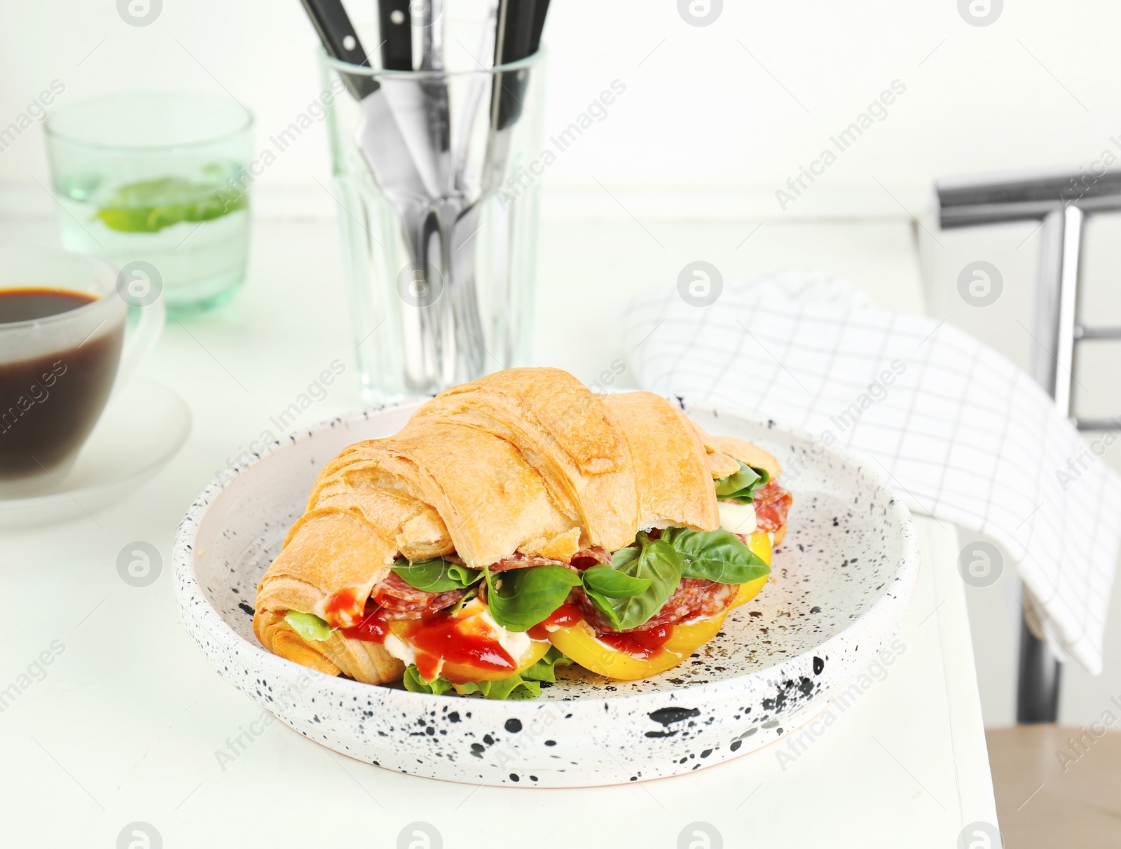 Photo of Tasty croissant sandwich with salami on table