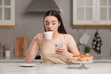 Photo of Woman using smartphone while having breakfast at table in kitchen. Internet addiction