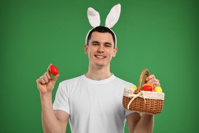 Photo of Easter celebration. Handsome young man with bunny ears and painted eggs on green background