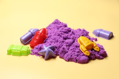 Violet kinetic sand and plastic toys on beige background