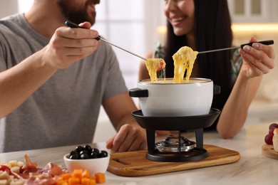 Couple enjoying cheese fondue during romantic date indoors, closeup