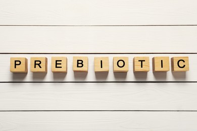 Photo of Wooden cubes with word Prebiotic on white table, flat lay