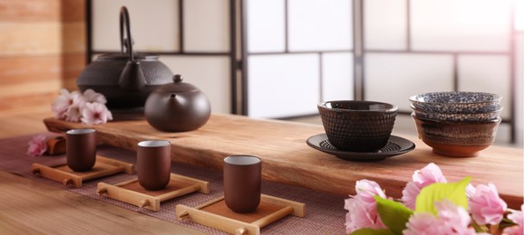 Image of Beautiful set for traditional tea ceremony and sakura flowers on wooden table. Banner design