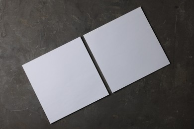 Blank paper sheets on dark textured background, top view. Mockup for design