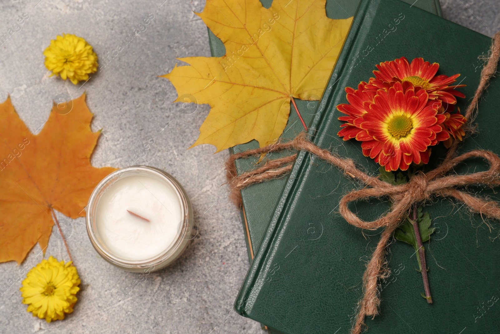 Photo of Book decorated with chrysanthemum flowers, autumn leaves and scented candle on light gray textured table, flat lay