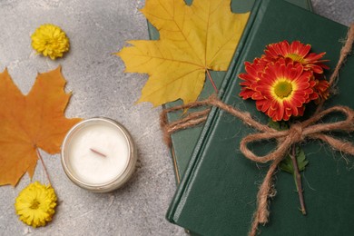 Photo of Book decorated with chrysanthemum flowers, autumn leaves and scented candle on light gray textured table, flat lay