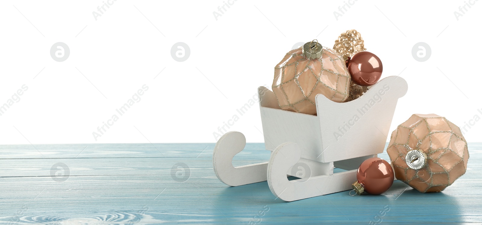 Photo of Decorative sleigh with Christmas ornaments on light blue wooden table. Space for text