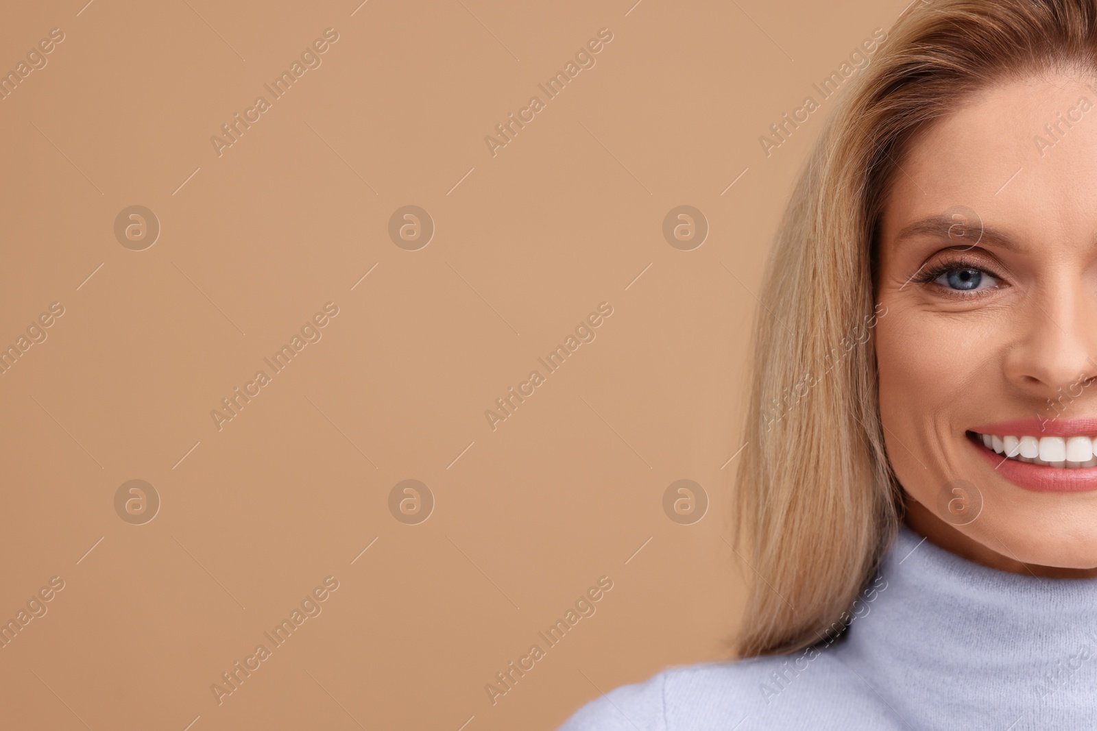 Photo of Portrait of smiling middle aged woman with blonde hair on beige background, closeup. Space for text