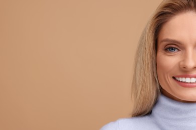 Portrait of smiling middle aged woman with blonde hair on beige background, closeup. Space for text