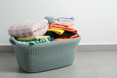 Photo of Plastic laundry basket with clean clothes on floor indoors. Space for text