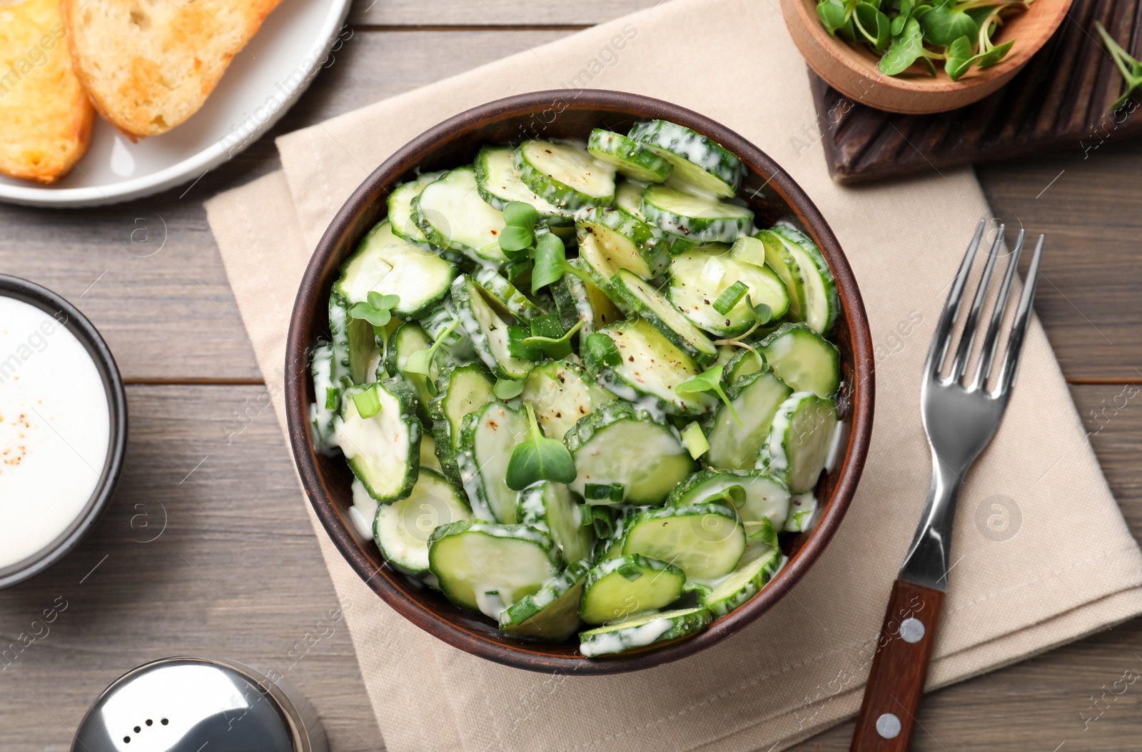 Photo of Bowl of delicious cucumber salad served on wooden table, flat lay