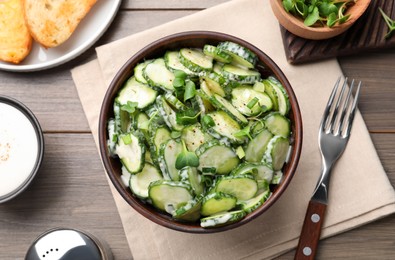 Bowl of delicious cucumber salad served on wooden table, flat lay