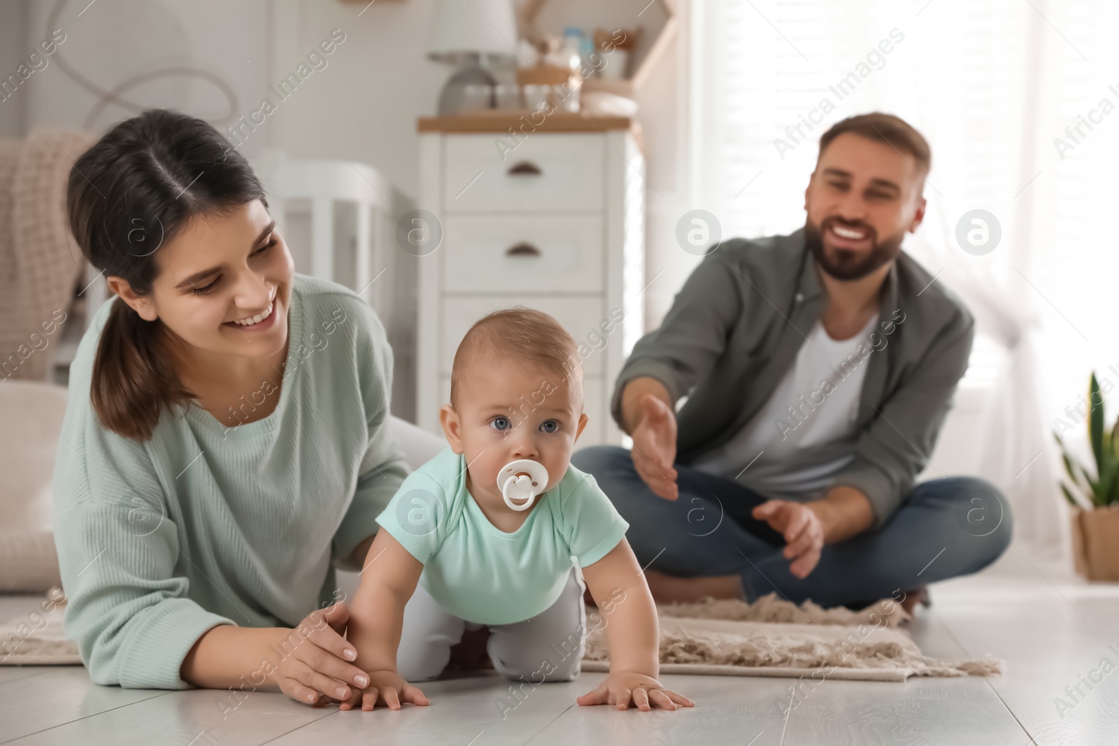 Photo of Happy parents helping their baby to crawl on floor at home