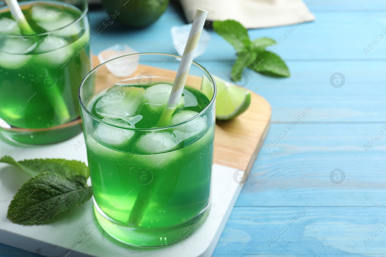 Photo of Delicious mint liqueur with green leaves and ice cubes on turquoise wooden table, closeup. Space for text