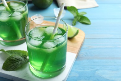 Delicious mint liqueur with green leaves and ice cubes on turquoise wooden table, closeup. Space for text