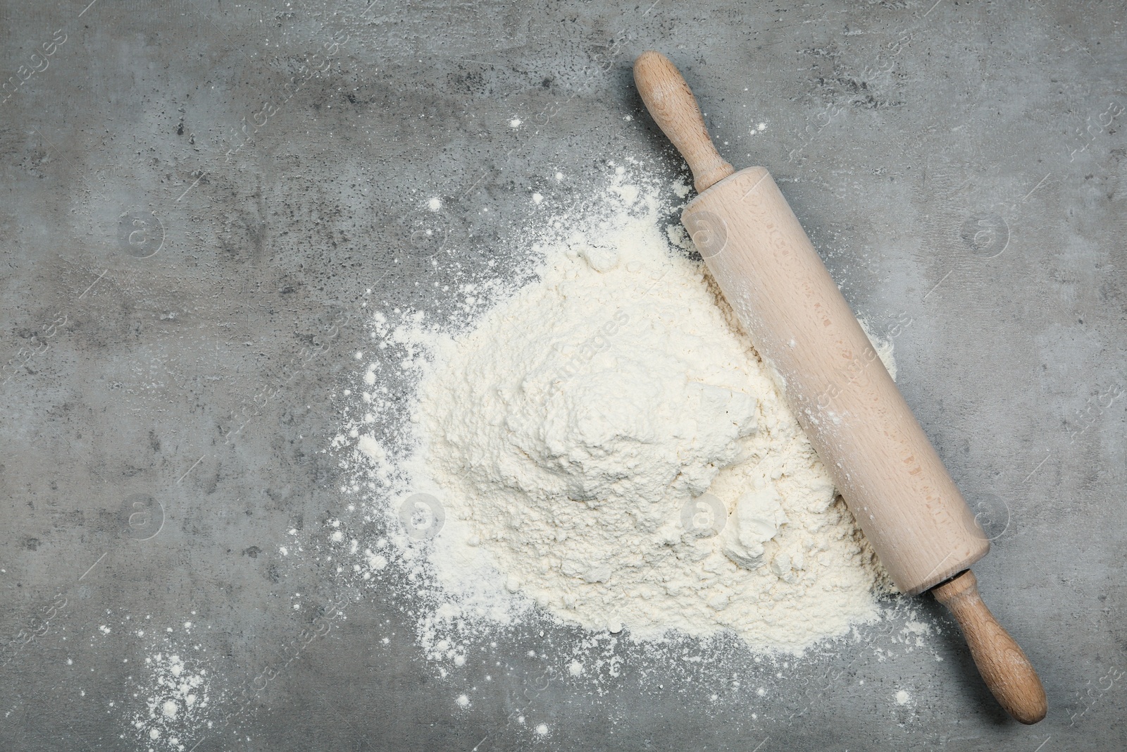 Photo of Flour and wooden rolling pin on light grey table, top view
