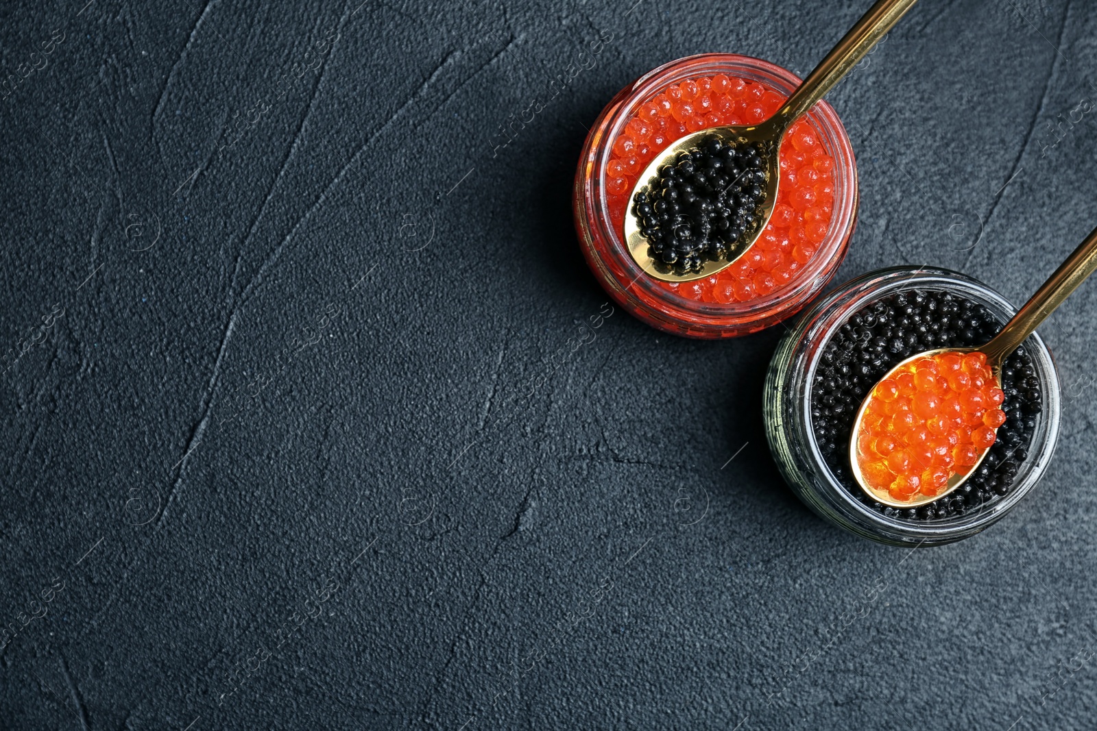 Photo of Glass jars and metal spoons with black and red caviar on grey background