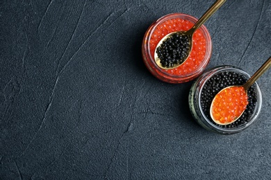 Glass jars and metal spoons with black and red caviar on grey background