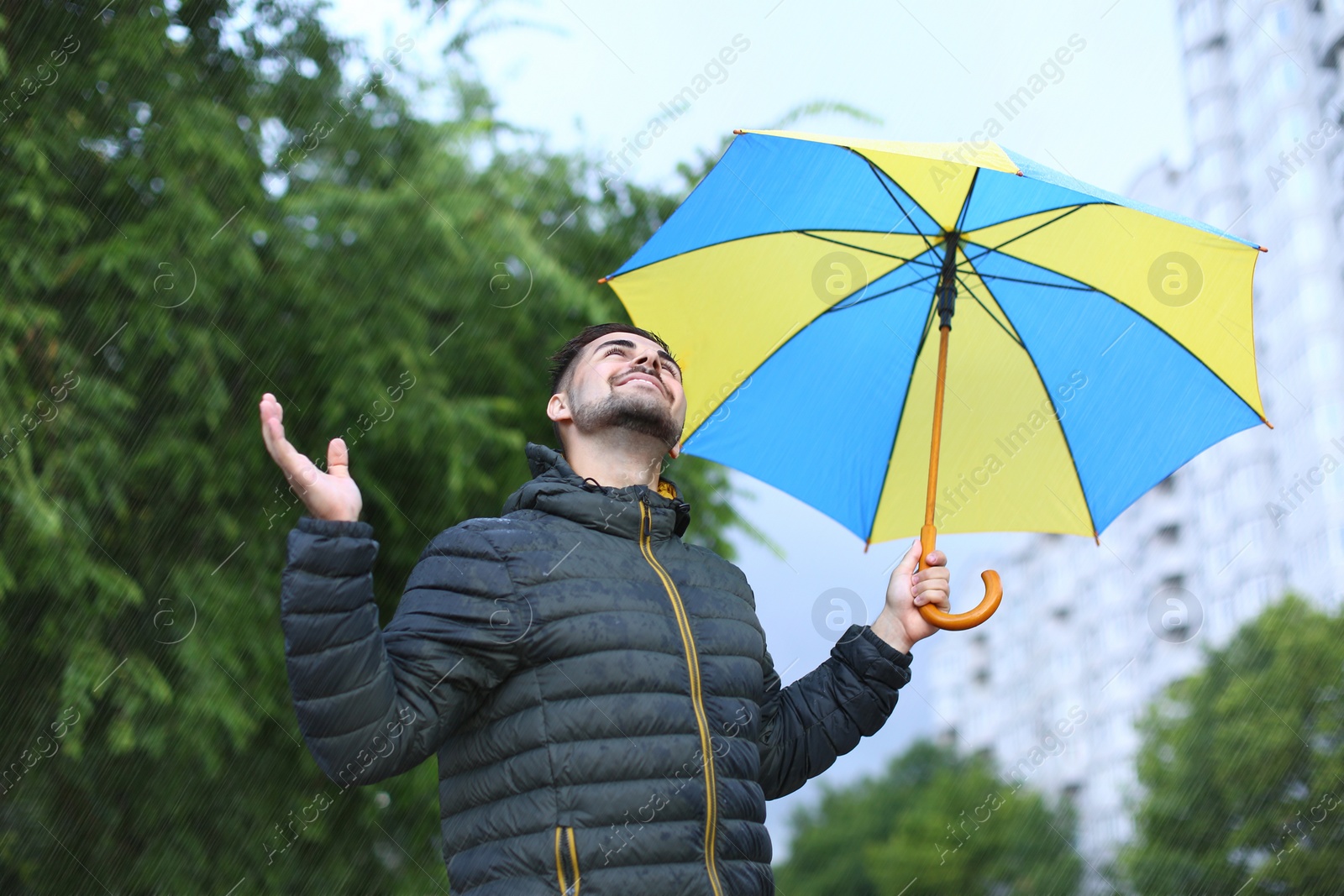 Image of Happy man with umbrella outdoors on rainy day 