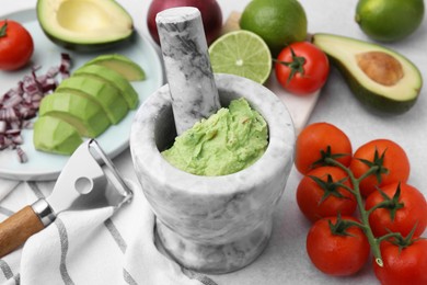 Mortar with delicious guacamole and ingredients on white table, closeup