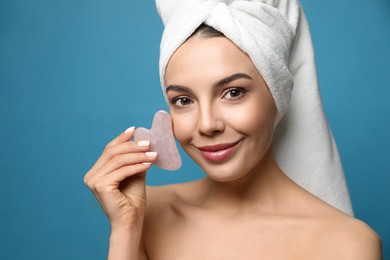 Photo of Beautiful young woman doing facial massage with gua sha tool on blue background