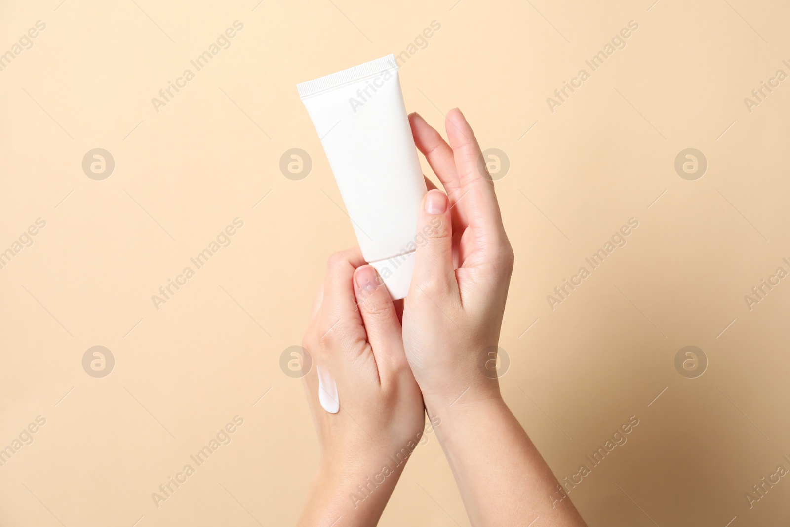 Photo of Woman with tube of hand cream on beige background, closeup