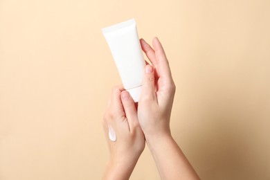 Woman with tube of hand cream on beige background, closeup