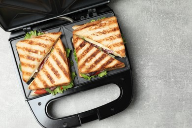 Modern grill maker with sandwiches on grey table, top view. Space for text