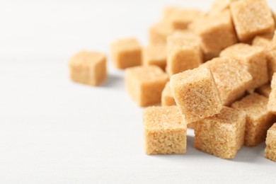 Photo of Heap of brown sugar cubes on white table, closeup. Space for text