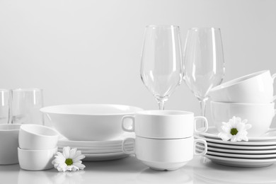 Photo of Set of many clean dishware, flowers and glasses on light table