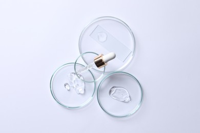 Photo of Petri dishes with samples of cosmetic serums and pipette on white background, flat lay