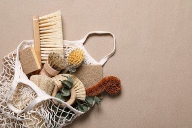 Photo of Cleaning brushes, sponges, eucalyptus and string bag on pale brown background, top view. Space for text