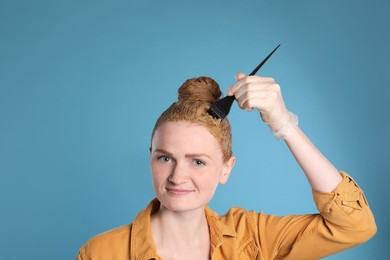Photo of Young woman dyeing her hair with henna on light blue background