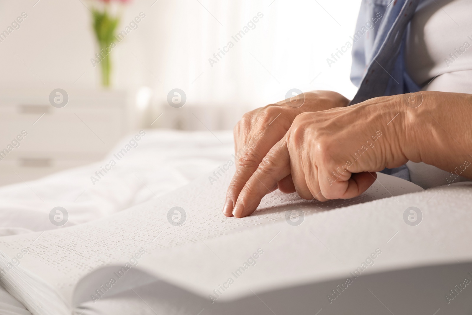 Photo of Blind senior person reading book written in Braille indoors, closeup