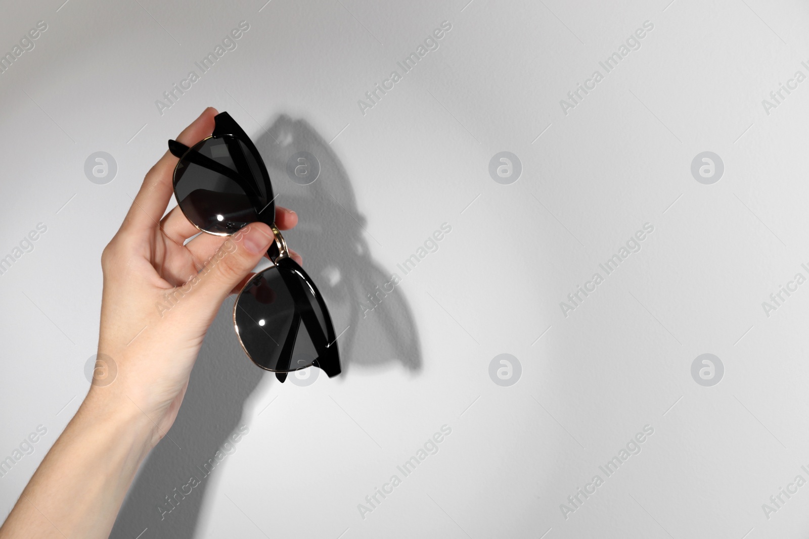 Photo of Woman holding stylish sunglasses on light background, closeup. Space for text