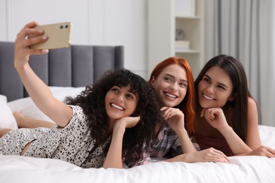 Happy young friends taking selfie on bed at home