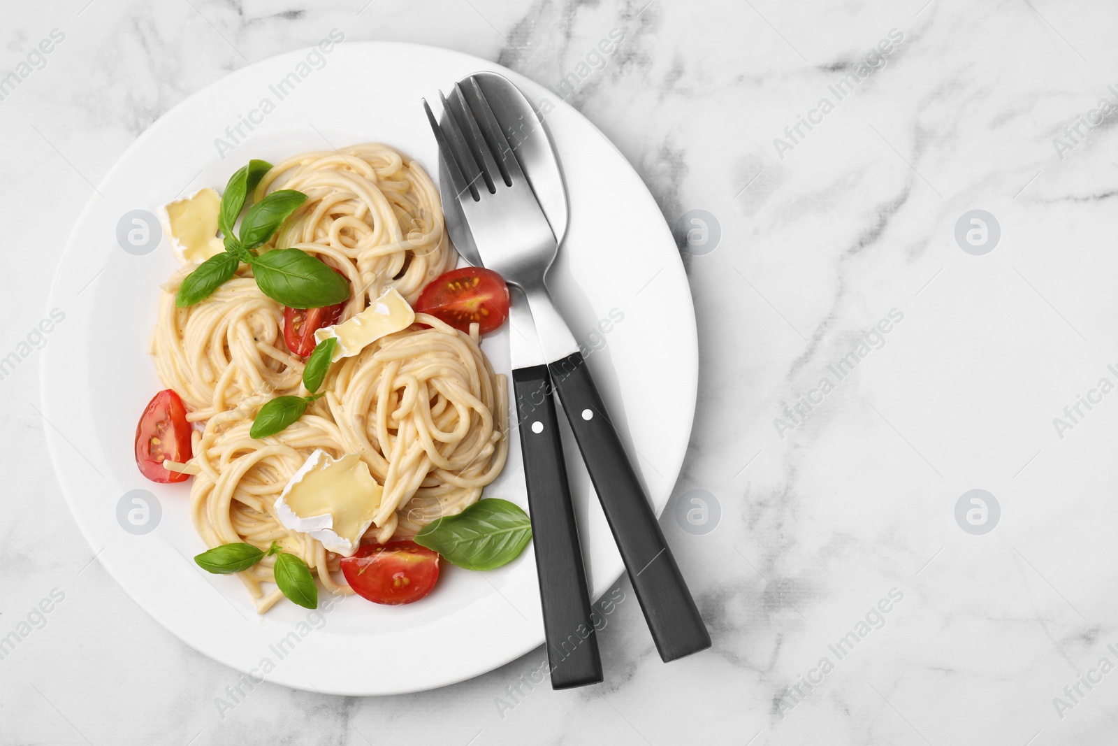 Photo of Delicious pasta with brie cheese, tomatoes, basil and cutlery on white marble table, top view. Space for text