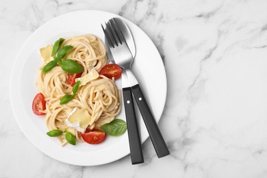 Delicious pasta with brie cheese, tomatoes, basil and cutlery on white marble table, top view. Space for text