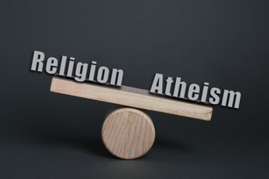 Image of Choice between atheism and religion. Miniature wooden seesaw with words on dark grey background