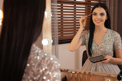 Beautiful young woman applying makeup near mirror in dressing room