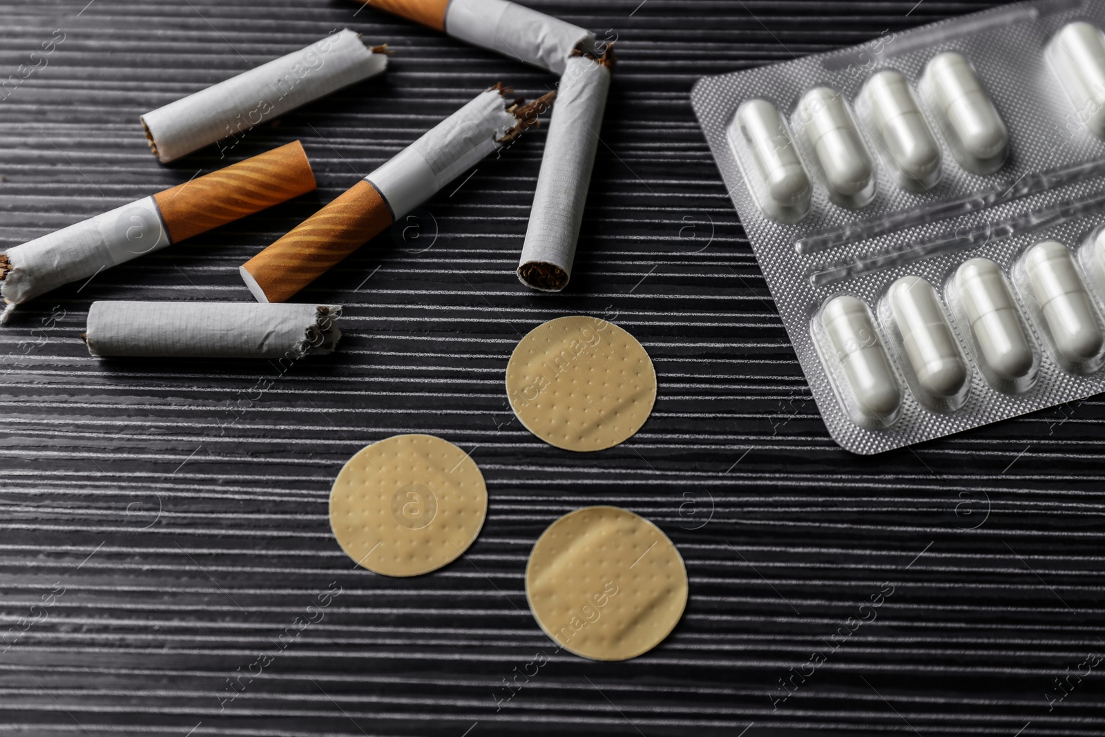 Photo of Nicotine patches, pills and broken cigarettes on black table, above view