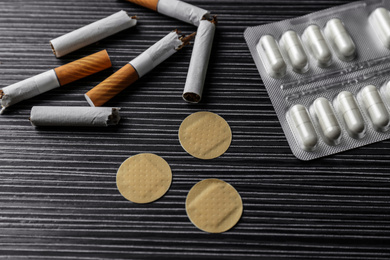 Photo of Nicotine patches, pills and broken cigarettes on black table, above view