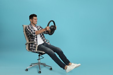 Happy man on chair with steering wheel against light blue background. Space for text