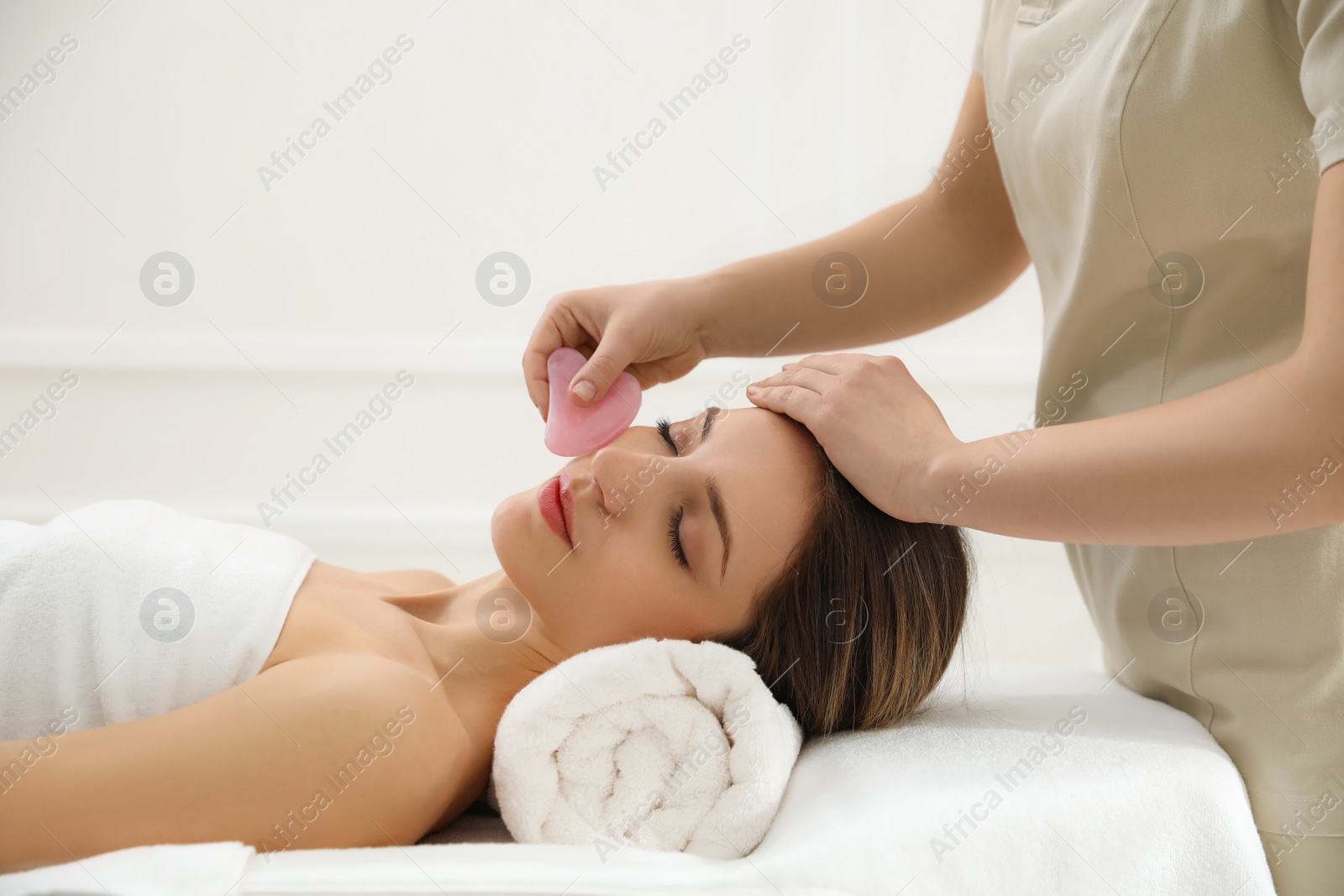 Photo of Young woman receiving facial massage with gua sha tool in beauty salon