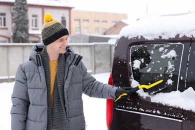 Man cleaning snow from car window outdoors